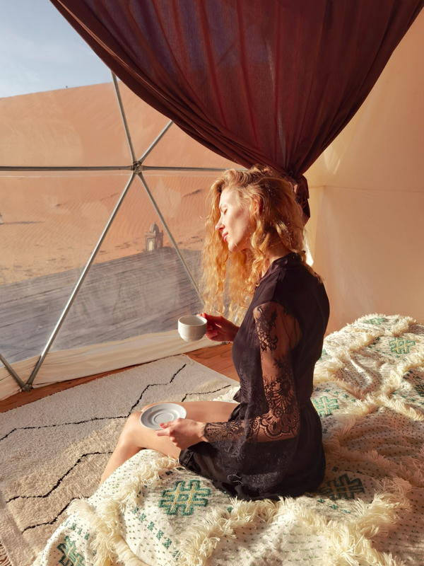 A young model enjoy her coffee in a dome tent at sunrise facing the Sahara Desert